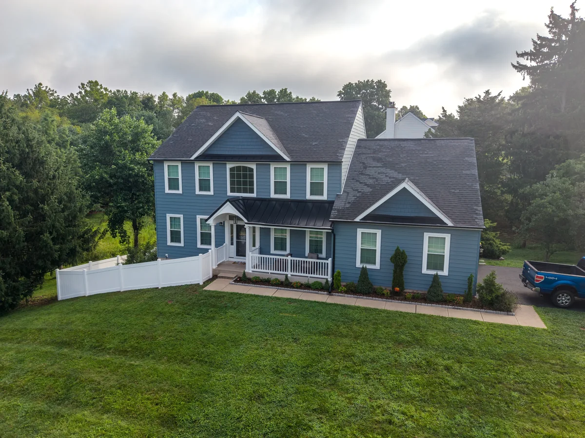 Aerial view of a blue two-story home, front lawn, and surrounding trees.