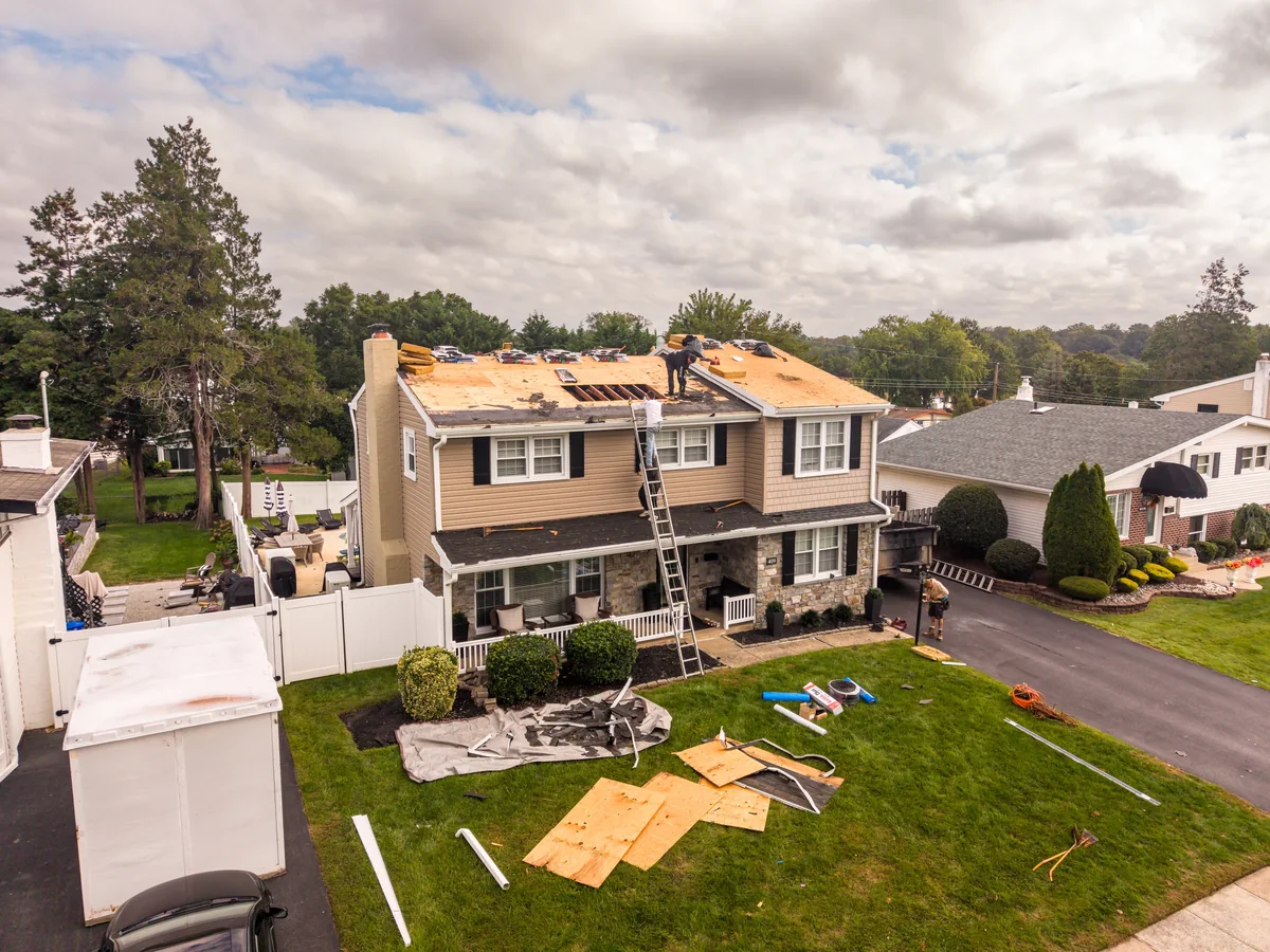 Aerial view of a residential roof replacement in progress, with materials on the roof and lawn.
