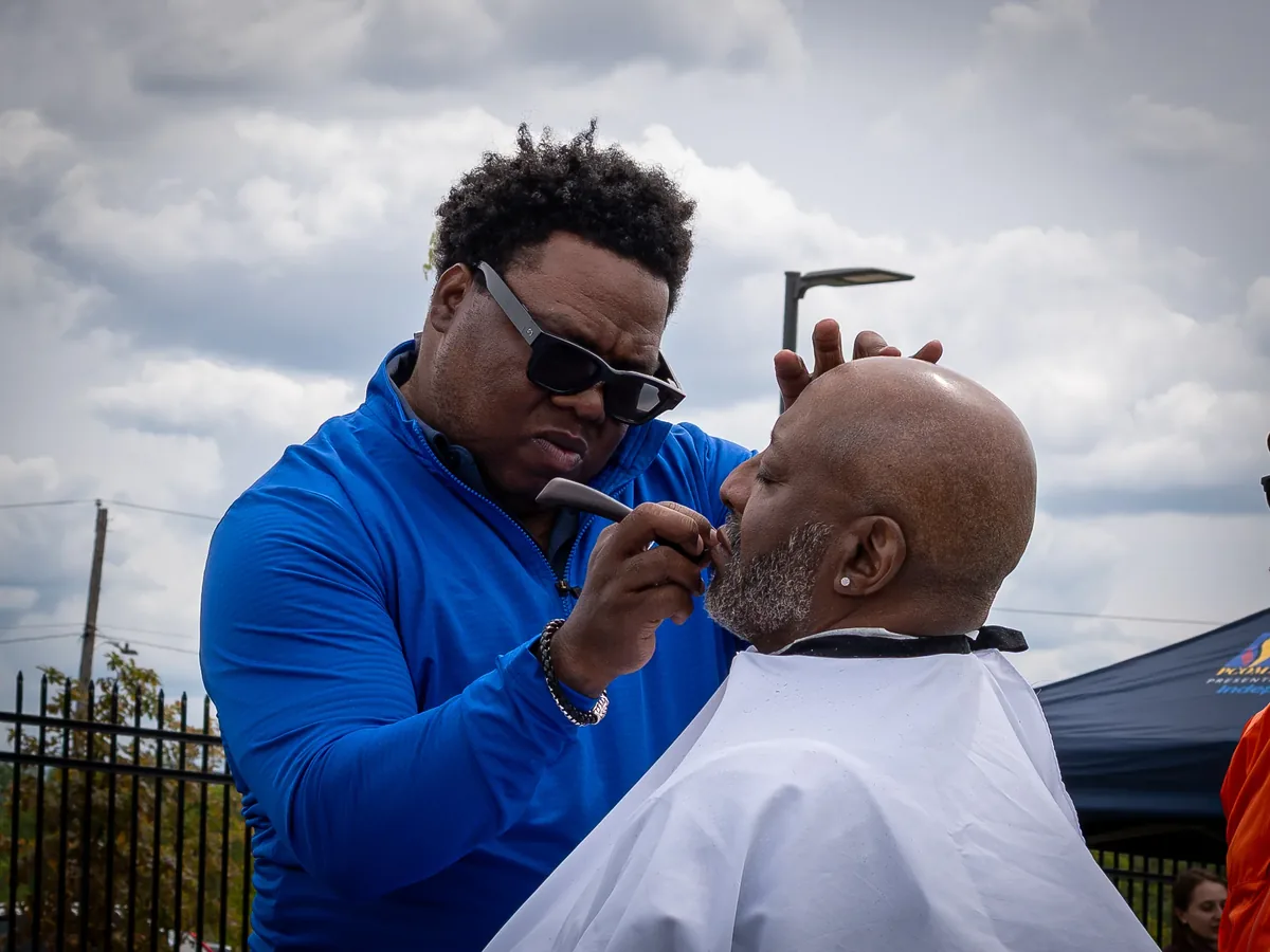A barber works with a customer at an outdoor community event.