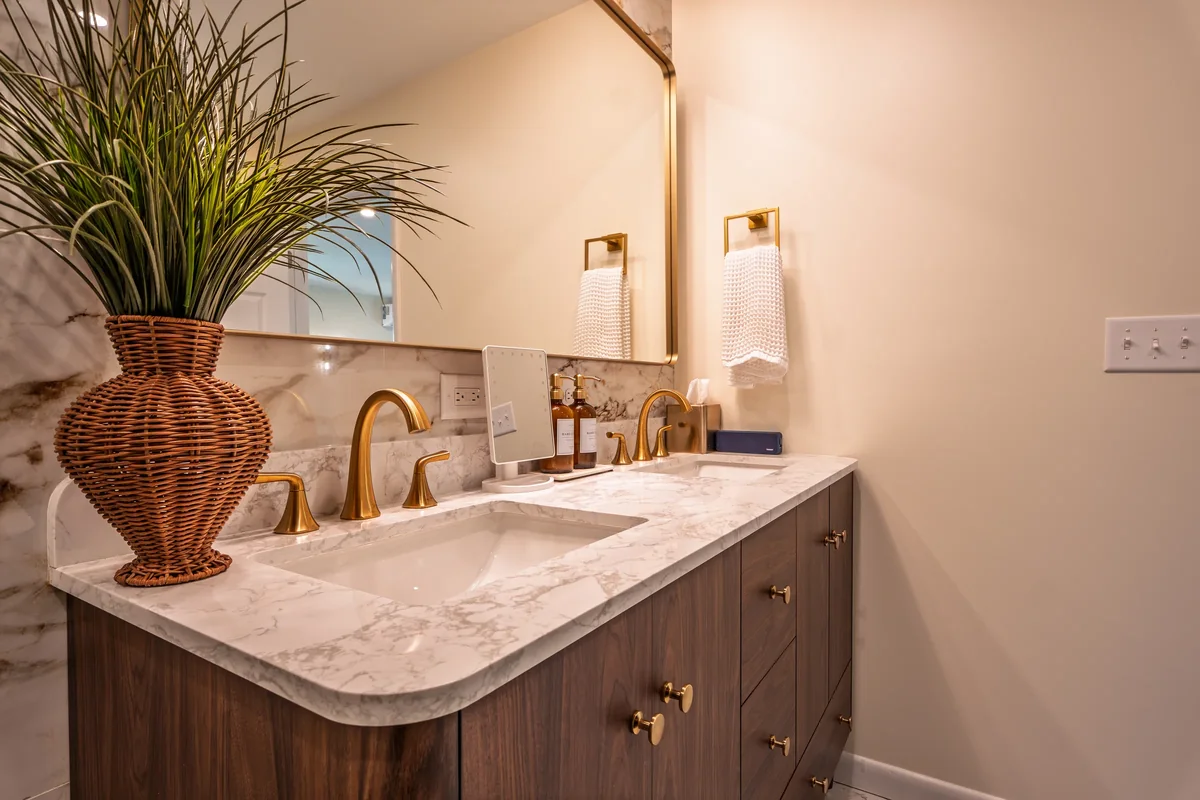 A bathroom vanity with a marble countertop, brass fixtures, and dark wood cabinetry.