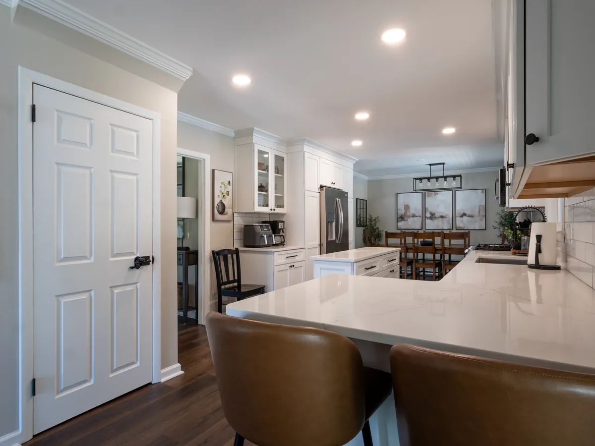 A renovated kitchen with white cabinetry, a stone island, and a dining area.