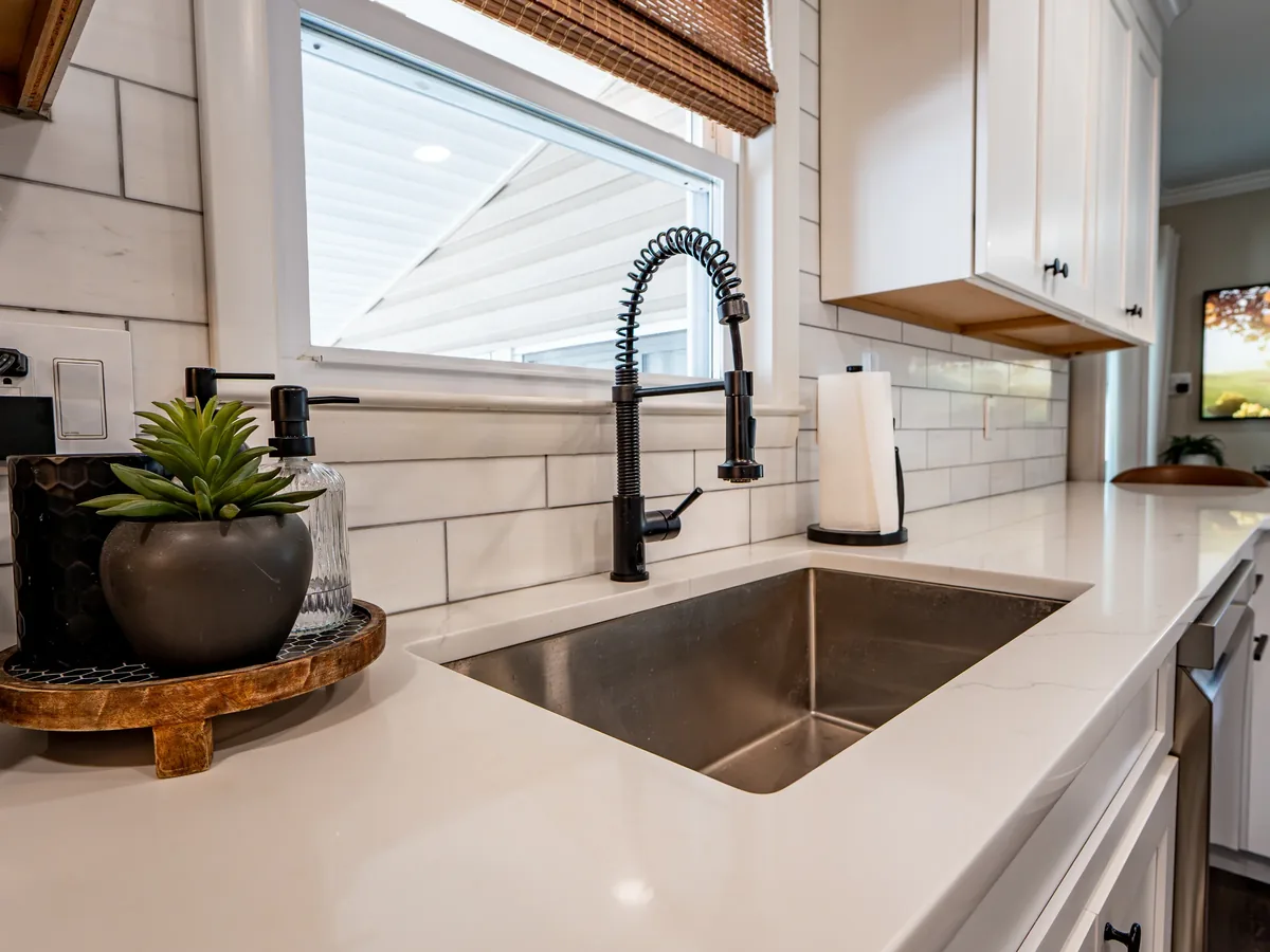 A stainless-steel kitchen sink beneath a window, with a tiled backsplash.