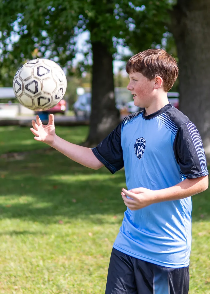 A young soccer player in a blue jersey tossing a soccer ball during outdoor practice.