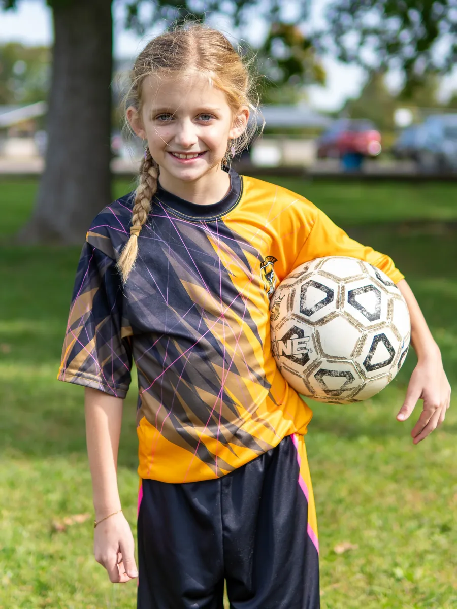 A young soccer player in a yellow jersey stands with a soccer ball.