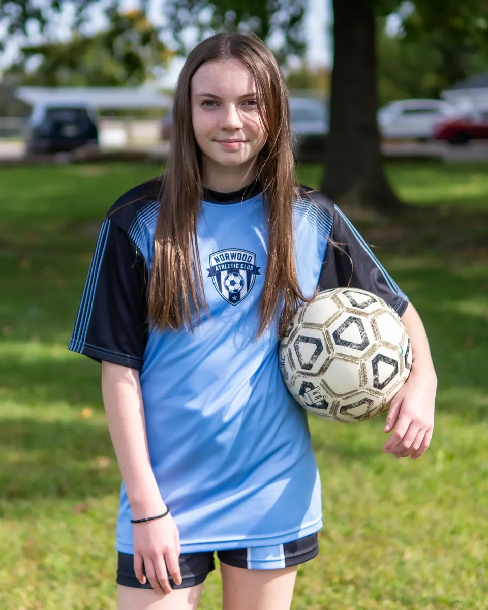 A young soccer player in a blue jersey holds a soccer ball.