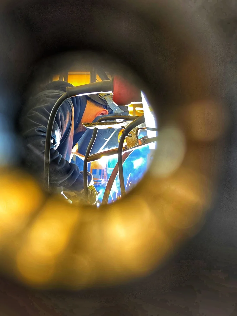 A welder works behind a metal frame, seen through its opening.